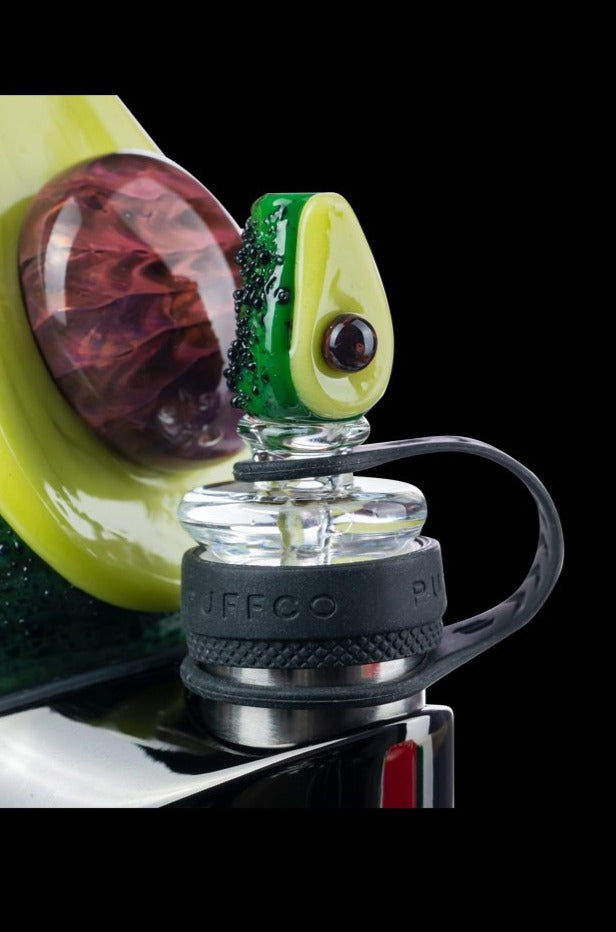 A close-up shot of the Empire Glassworks Avocadope Carb Cap for Puffco Peak, displaying a green, avocado-shaped design against a dark backdrop.