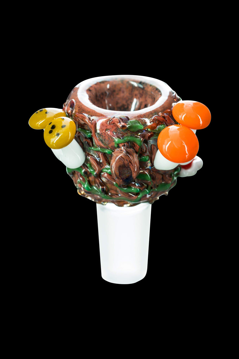 Close-up front view of the Empire Glassworks "Bug's Life" Bowl showing a textured brown nest-like glass cup with green vine accents and small yellow and orange mushroom decorations against a black background