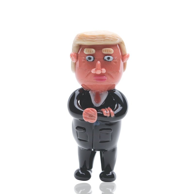 Front view of the Empire Glassworks “Agent Orange” Trump hand pipe, a sculpted, orange-toned figurine presented on a plain white background.