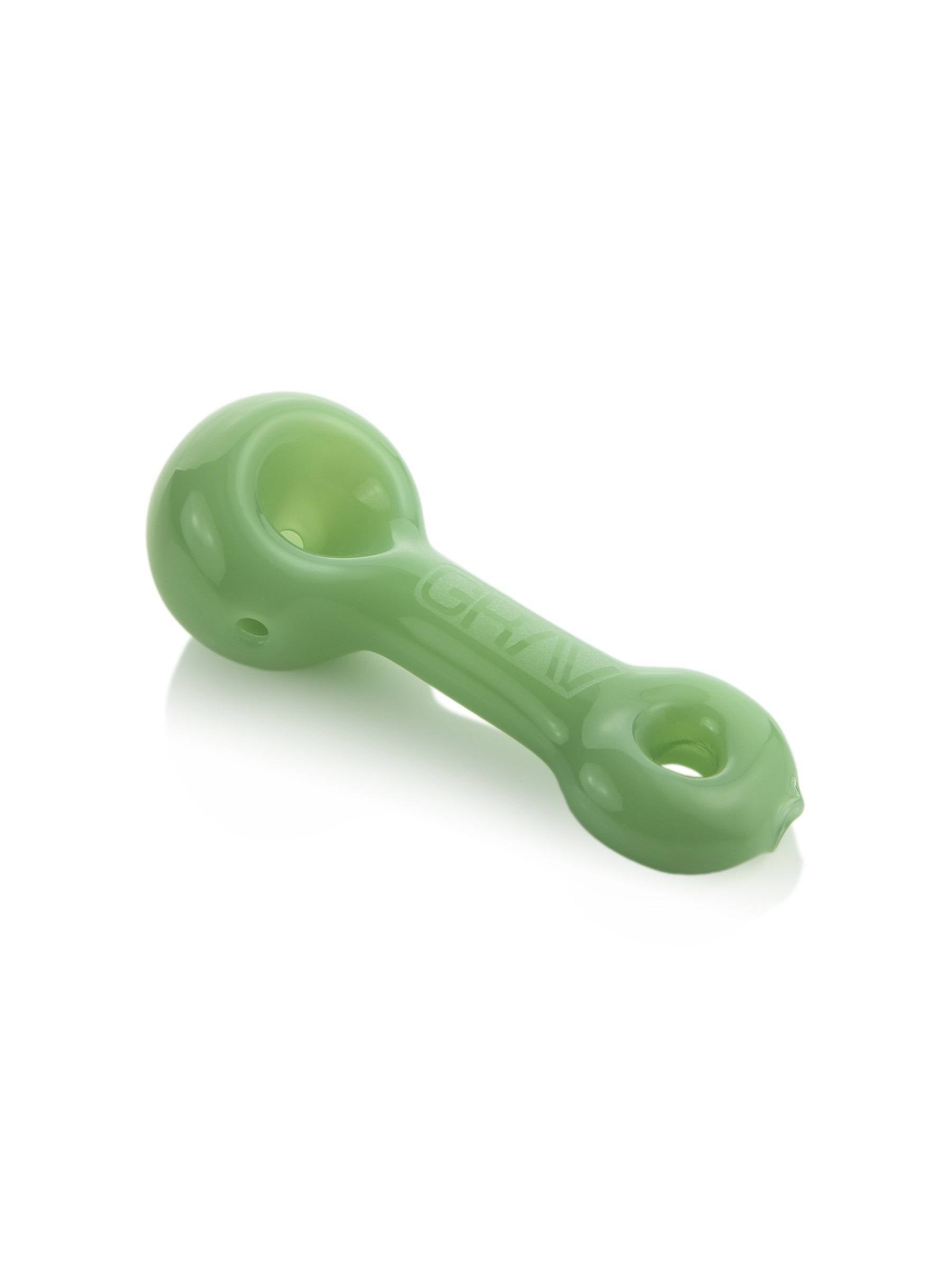 Angled close-up of a pale green GRAV® Mini Spoon Pipe on a white reflective surface, showing the bowl and logo.