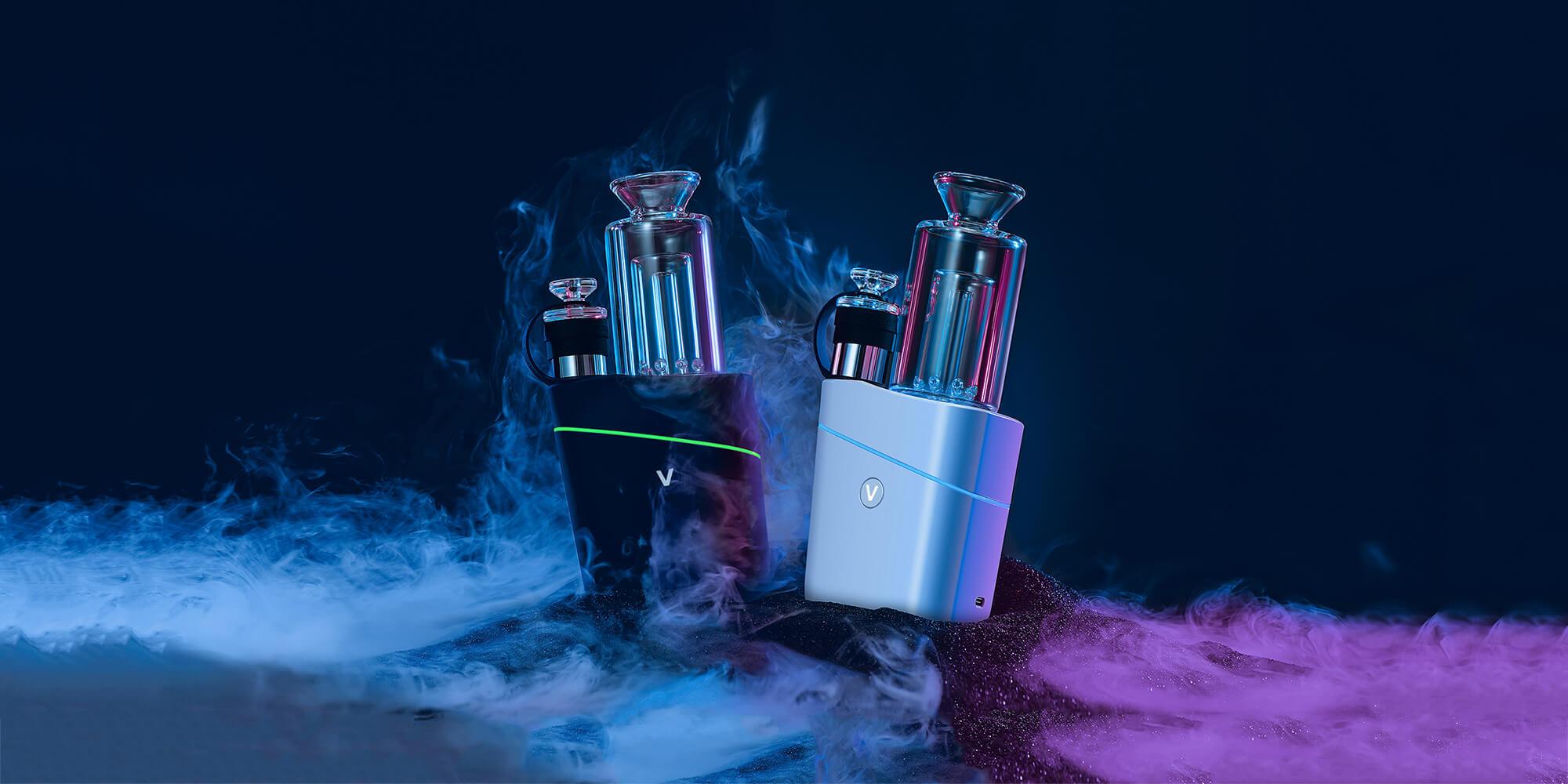 Three-quarter view of two VLAB Halo V2 Smart E-Rig units—one black and one white—lit by blue and magenta highlights with smoky vapor around them.