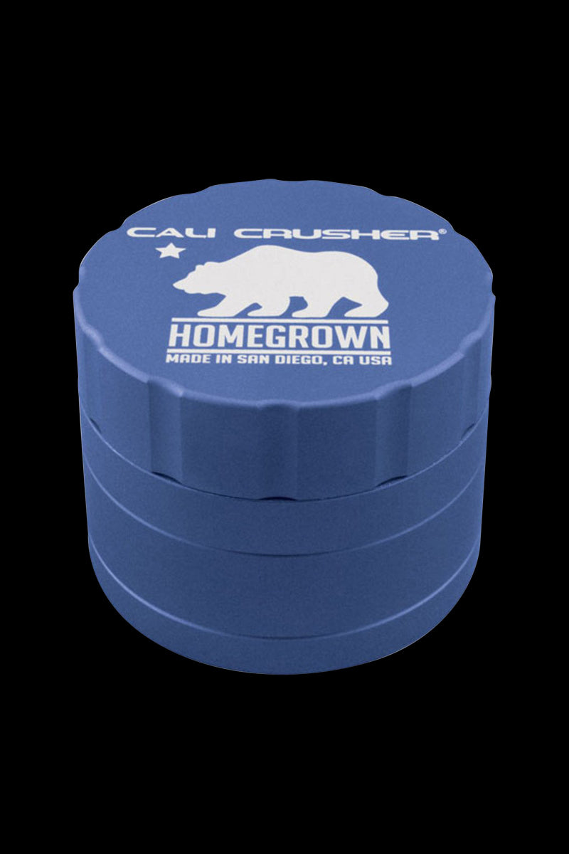 Angled top-down view of a blue Cali Crusher Homegrown 4-Part Grinder showing its stacked tiers and white bear logo on a black background.