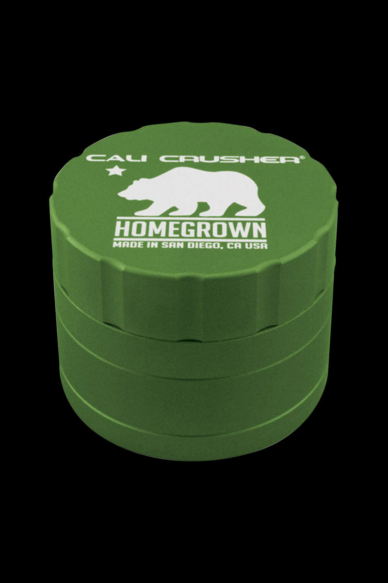 Close-up front-angle view of a green Cali Crusher Homegrown 4-Part Grinder with white bear logo and text on its textured lid against a black background