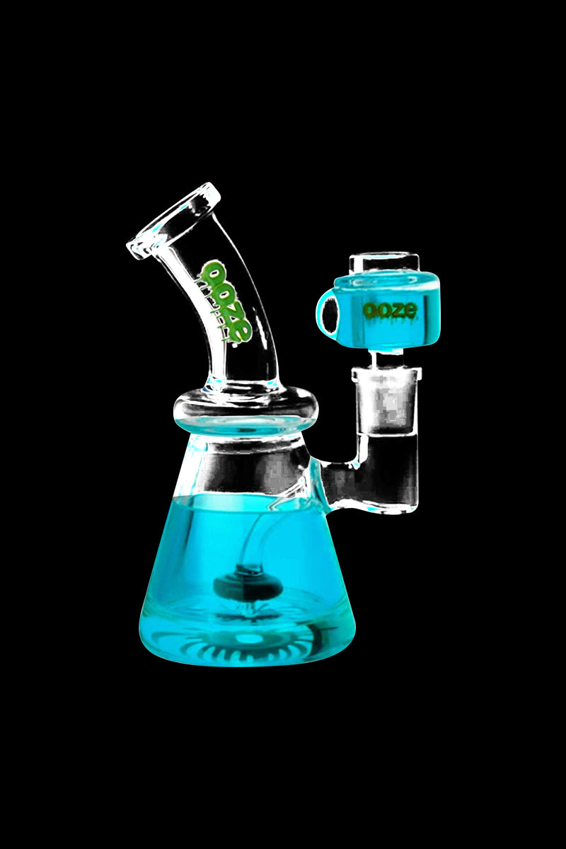 Angled front view of an Aqua Teal Ooze Glyco Glycerin Chilled Bong against a black background, showing its beaker base partly filled with turquoise liquid and a matching teal carb cap.