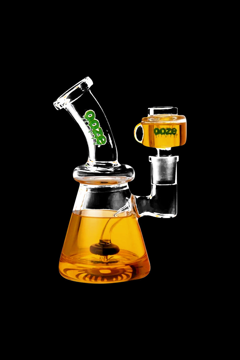 Three-quarter front view of an Ooze Glyco Glycerin Chilled Bong with amber liquid in its beaker base and green Ooze logo on the neck.