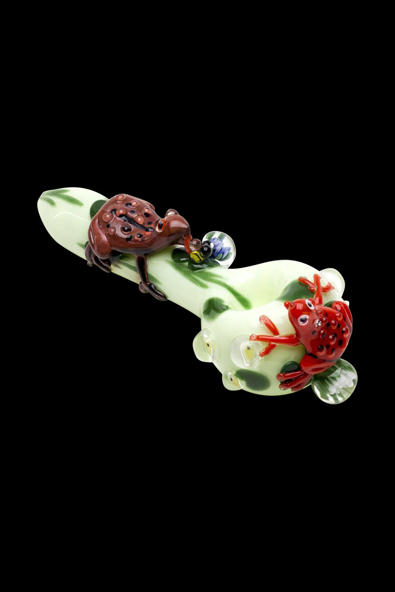 Angled close-up of the Empire Glassworks Ribbit Small Spoon Pipe showing two glass frogs on a pale green spotted body against black.