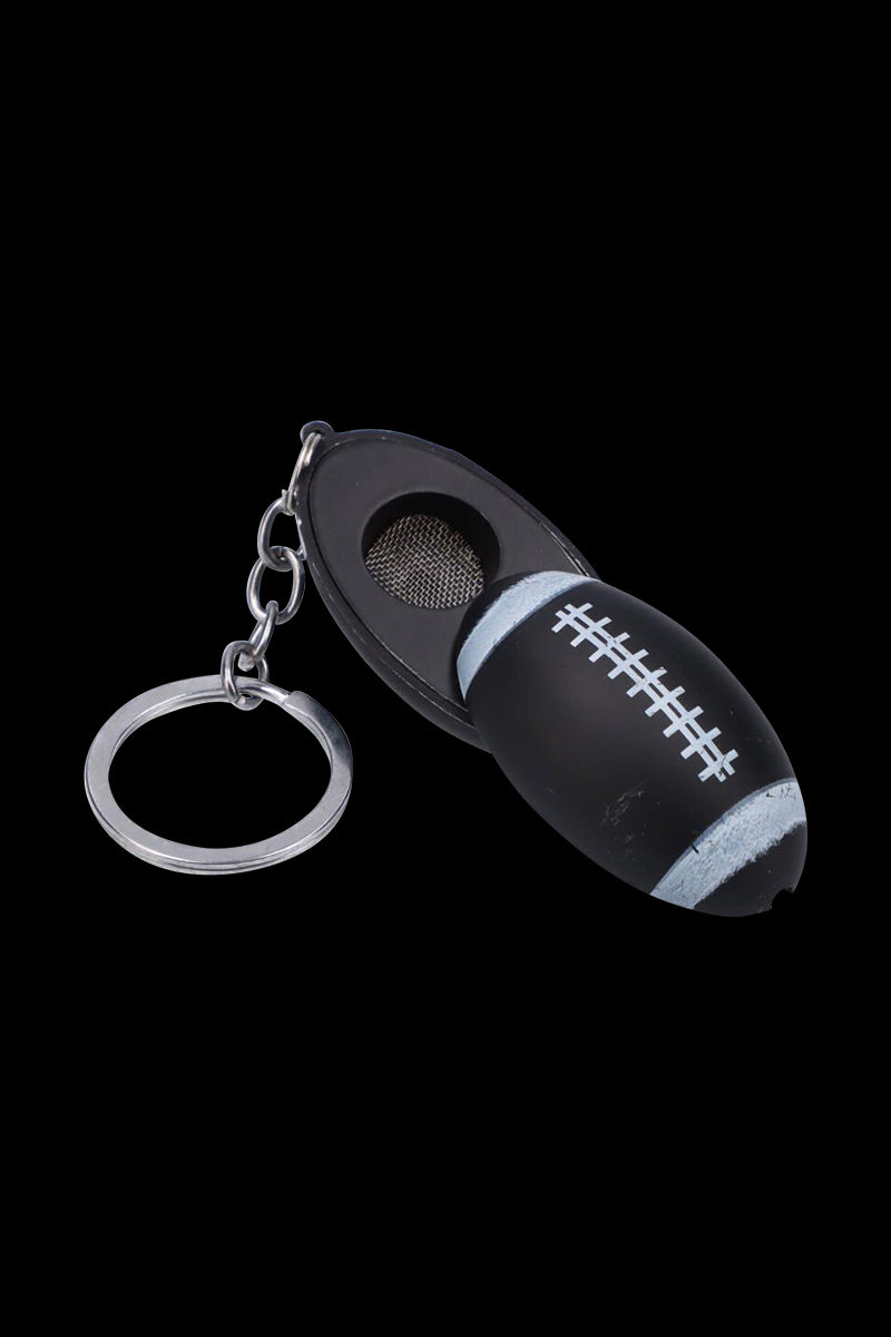 Angled close-up of the American Football Metal Hand Pipe with Key Chain showing a black football-shaped pipe, silver laces, mesh bowl and metal key ring on a black background.