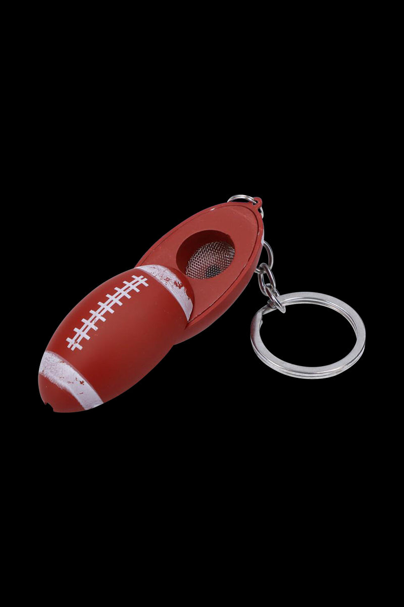 Close-up angled view of the American Football Metal Hand Pipe with Key Chain showing a red football-shaped metal pipe with white laces, mesh bowl, and attached silver key ring against a black background.