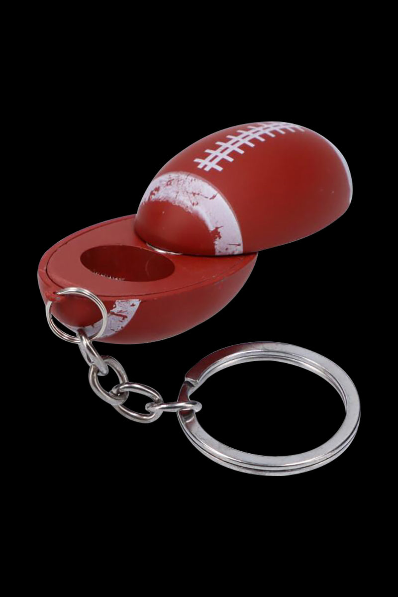 Angled close-up of the American Football Metal Hand Pipe with Key Chain showing a red, football-shaped metal body split open to reveal the bowl and attached silver key ring.