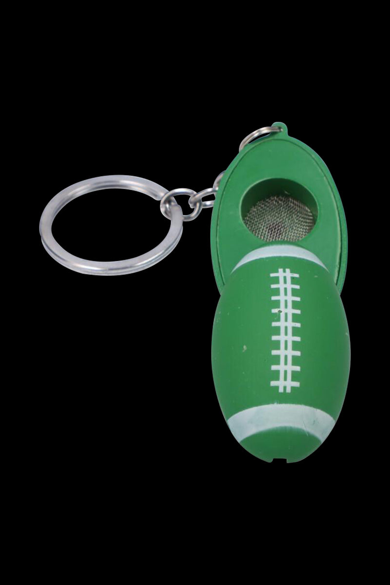 Diagonal close-up of the American Football Metal Hand Pipe with Key Chain showing a green football-shaped body, open hinged bowl and attached silver key ring on a black background.