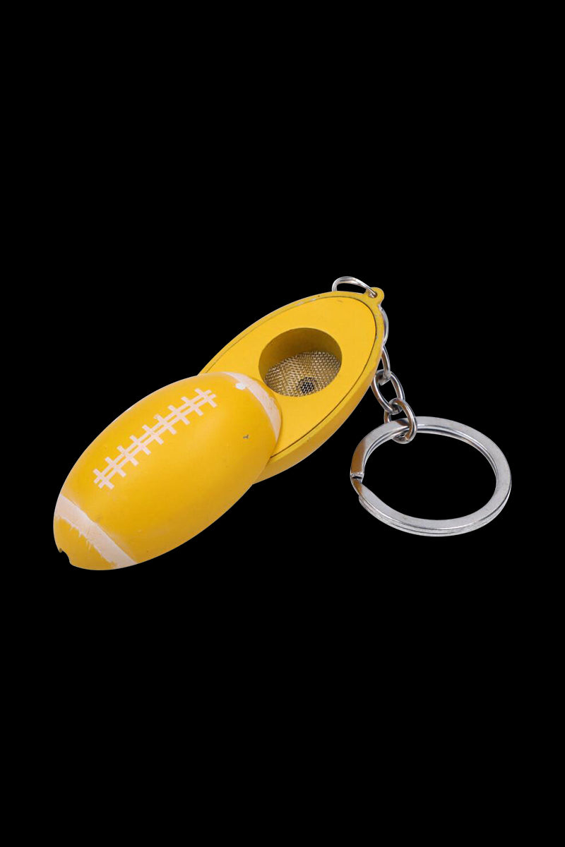 Close-up of the American Football Metal Hand Pipe with Key Chain in yellow shaped like a football with its hinged bowl exposed against a black background