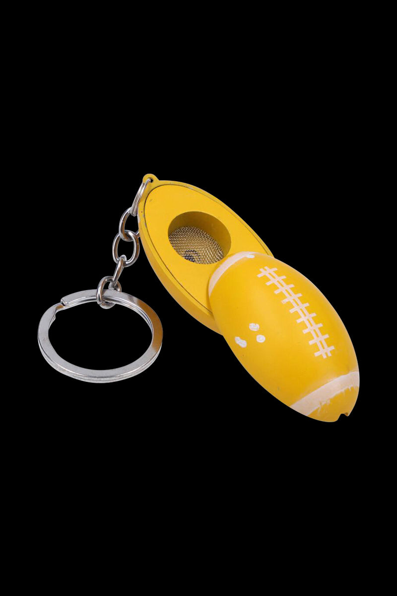 Close-up of an open American Football Metal Hand Pipe with Key Chain in bright yellow showing its metal screen bowl and silver split-ring chain against a black background.