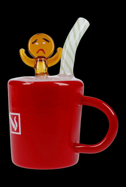 Red glass mug with a sculpted, sad gingerbread man figure emerging from the top, and a striped glass straw; cannabis accessory.