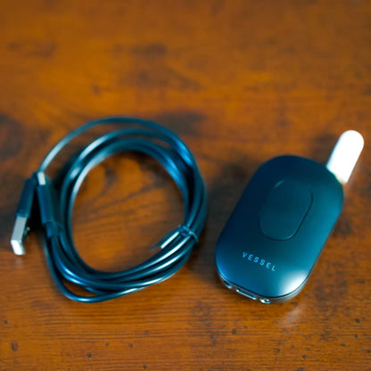 Top-down close-up of the Freeze Pipe Vape Pen on a warm wooden surface, showing its coiled cable and matte body.
