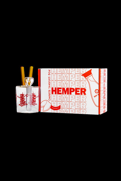 A glass bubbler pipe inside a Chinese takeout-style box branded with “Hemper” and cannabis leaf designs.