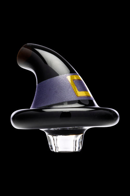 A glass dab cap shaped like a witch’s hat, with a dark purple and black speckled pattern and a gold accent, against a black background.