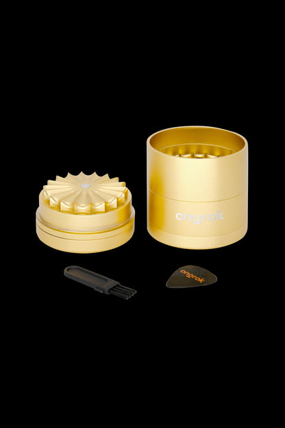 Gold cannabis grinder with cleaning brush and scraper on a white background.