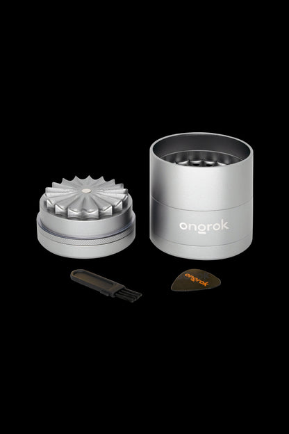 Silver cannabis grinder with components displayed, including a cleaning tool and collection dish, branded "ongrok."