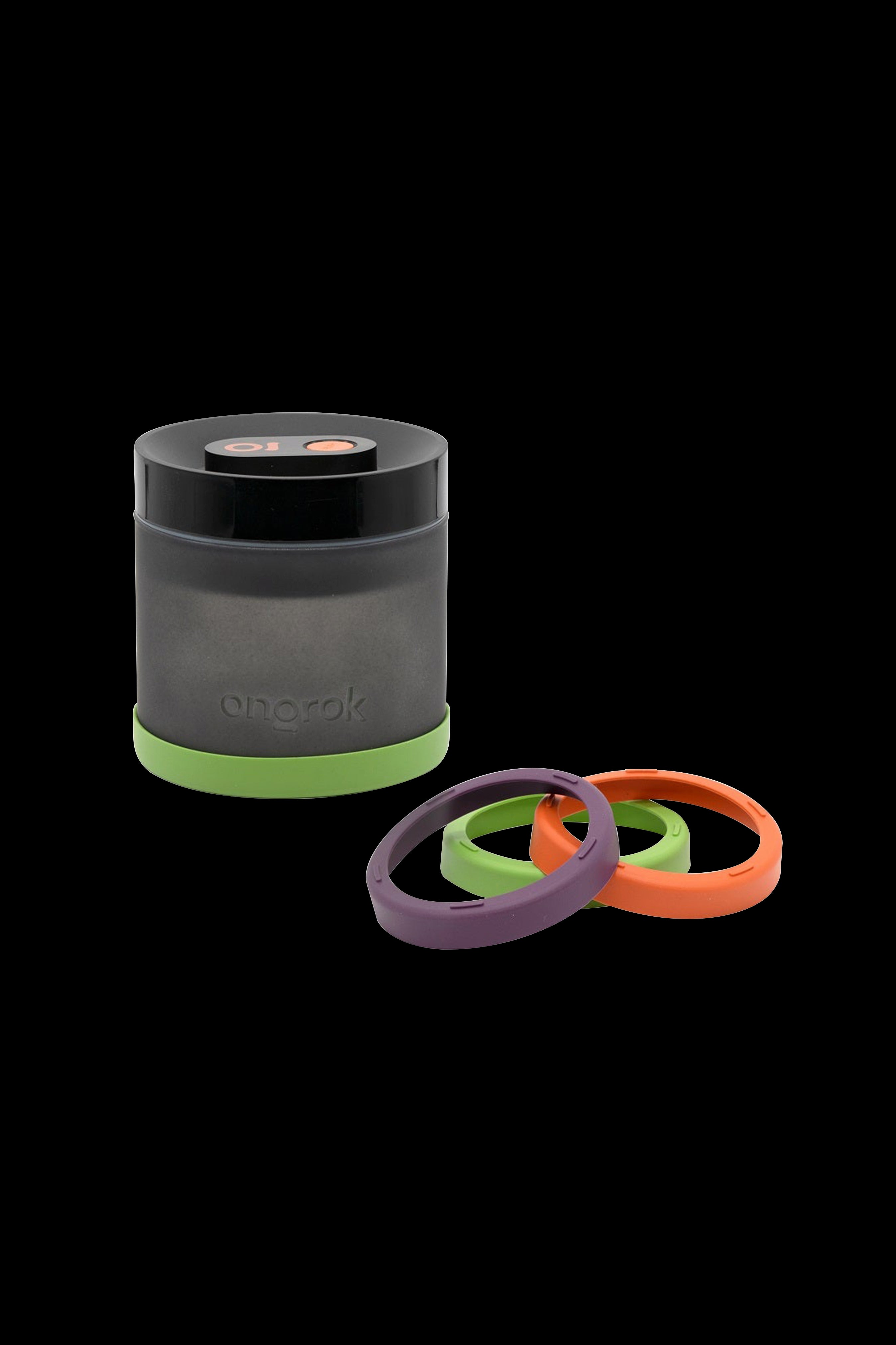 A gray cannabis storage container with a green silicone ring base and three additional silicone rings in green, purple, and orange beside it.