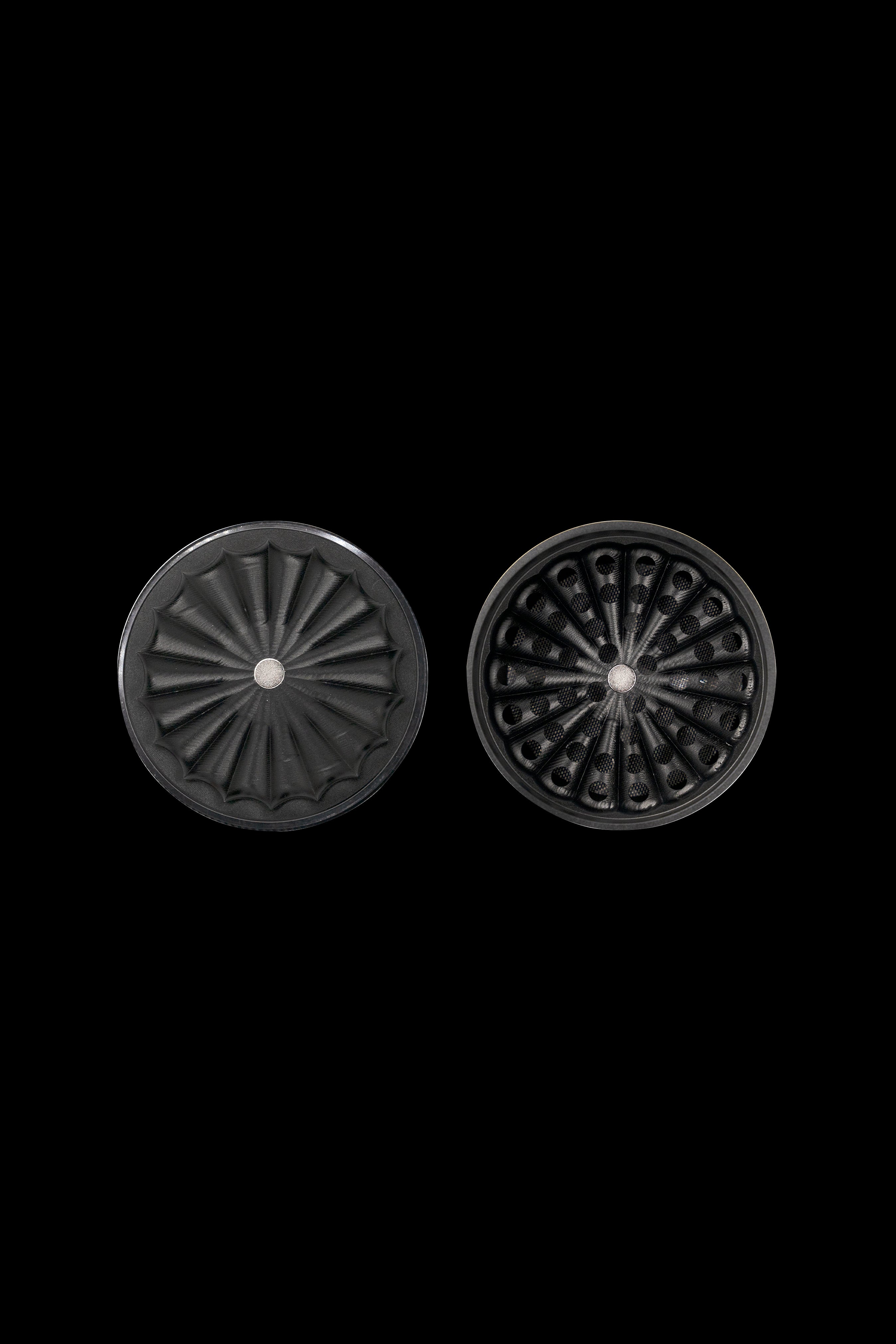 Two dark, intricately designed cannabis grinder plates against a black background.