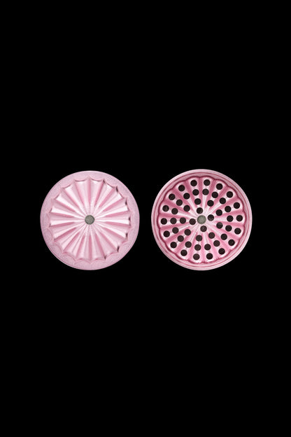 Pink cannabis grinder parts with textured and perforated surfaces on a black background.