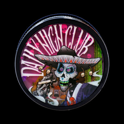 Close-up top view of a circular Black Skull Mini Travel Grinder lid showing a colorful Day-of-the-Dead skull in a sombrero against radiating pink and white stripes.