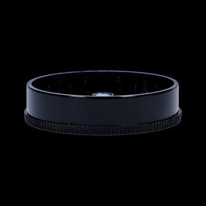 Low-angle close-up of the Black Skull Mini Travel Grinder showing its glossy black rim, interior teeth, and textured base against a black background