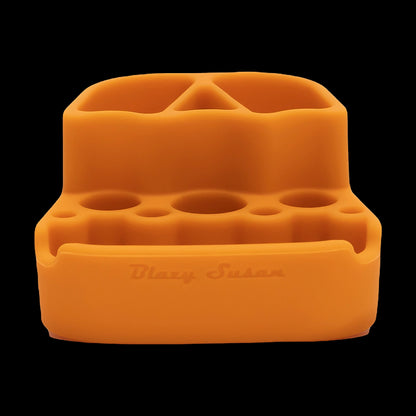 Close-up front view of the orange Blazy Susan Dab Station showing its molded silicone wells and slots against a black background.