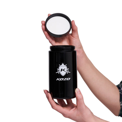 A hand holds a black airtight container with a cannabis leaf-shaped logo and the text "KOZO" printed on it.