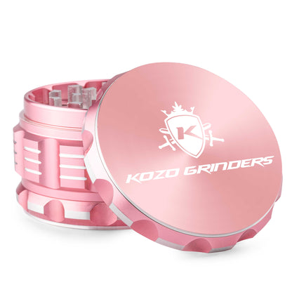 Pink metal cannabis grinder with "KOZO GRINDERS" logo, partially open to reveal the grinding teeth.