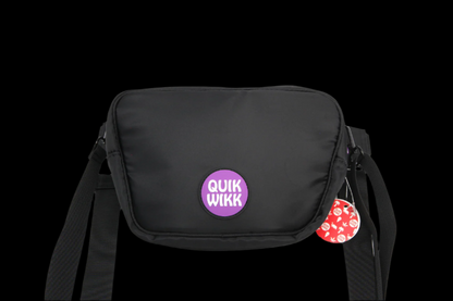 Front-facing shot of a black Quik Wikk Fanny Pack with a centered purple circular logo and visible shoulder straps.