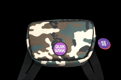 Front-facing view of a camo Quik Wikk Fanny Pack with a centered purple round logo and black straps against a black background