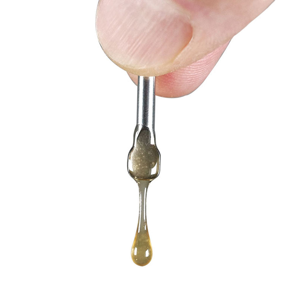 Close-up of a finger holding a RYOT® 3 Pack Of Extra Coils For 710 Wax Tank - New coil tip with a honey-colored droplet stretching downward against a white background