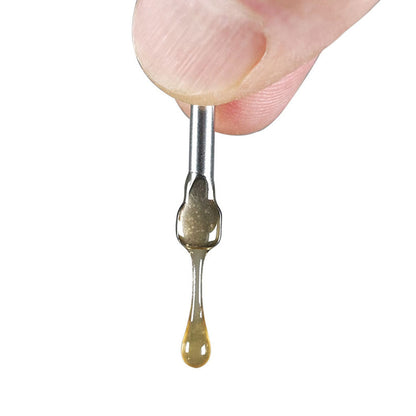Close-up of a finger holding a RYOT® 3 Pack Of Extra Coils For 710 Wax Tank - New coil tip with a honey-colored droplet stretching downward against a white background