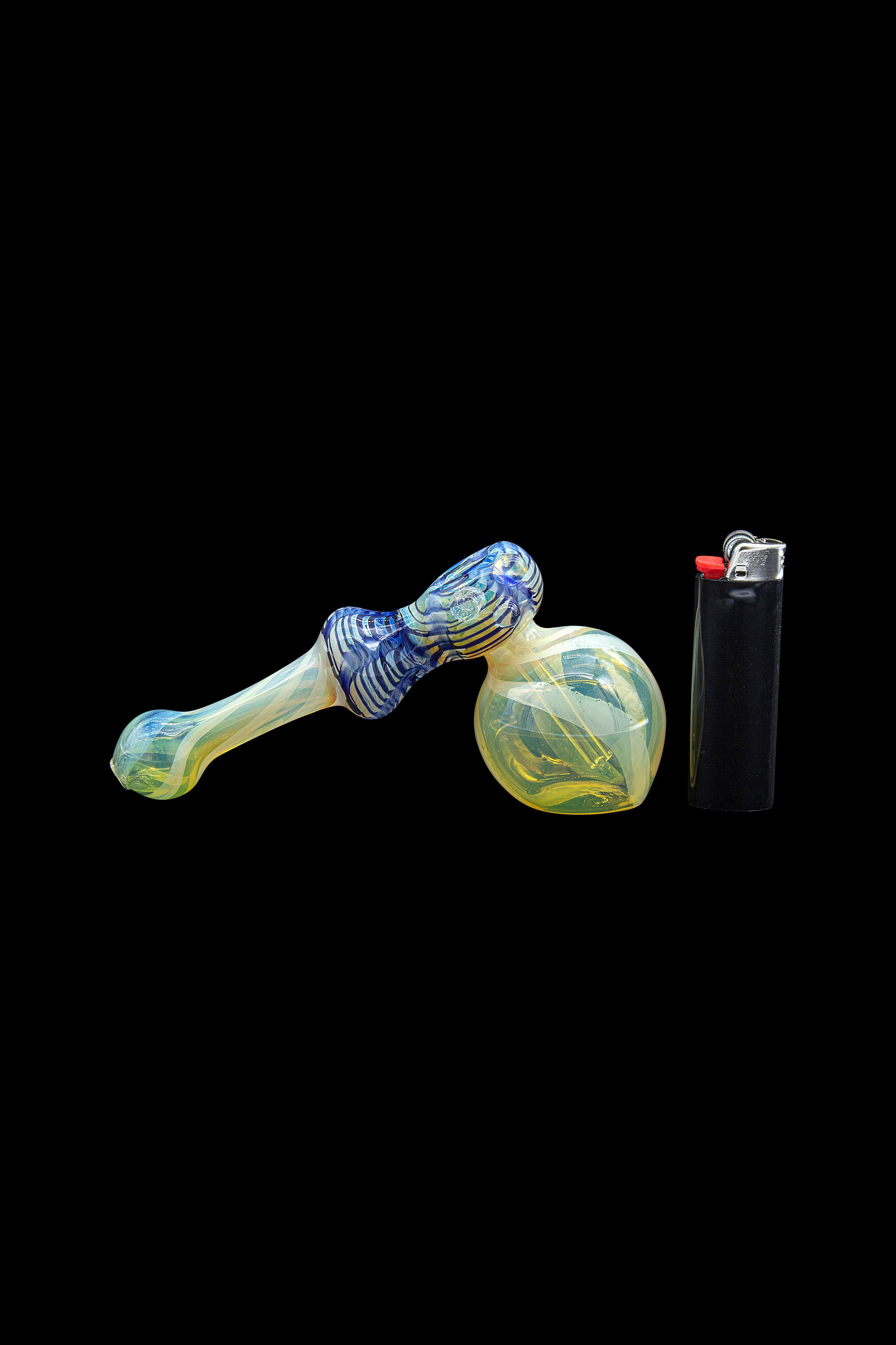 Hand-blown glass bubbler pipe with blue and yellow swirls, next to a black lighter on a black background.
