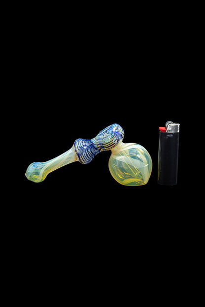 Hand-blown glass bubbler pipe with blue and yellow swirls, next to a black lighter on a black background.
