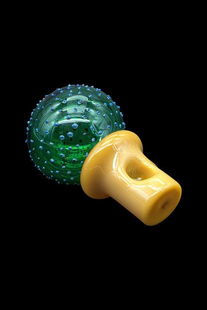 Green textured glass sphere with a yellow mushroom-shaped glass pipe resting beside it on a black background.
