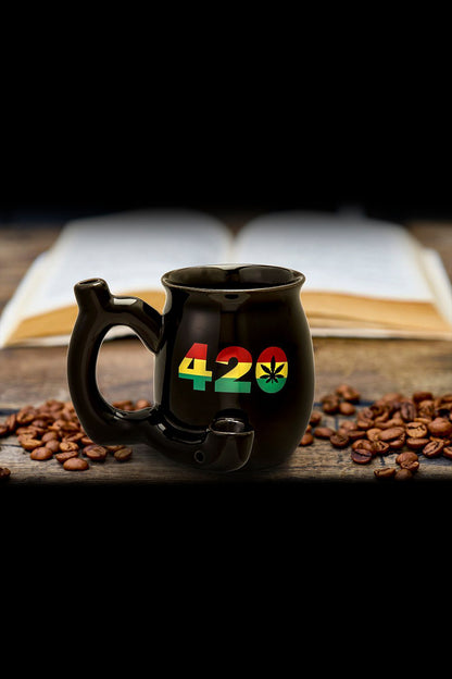Black ceramic mug with "420" and a cannabis leaf design, surrounded by coffee beans on a wooden surface.