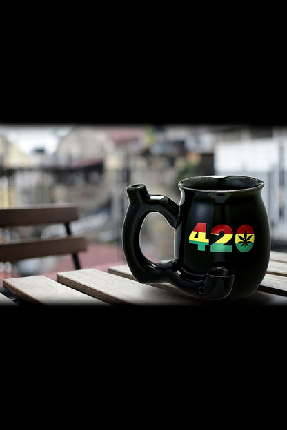Black ceramic mug with “420” and a marijuana leaf design, sitting on a wooden table with a blurred outdoor background.