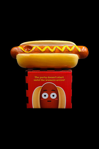 A hot dog rests on top of a red box with a cartoon hot dog face and text reading "The party doesn't start until the wieners arrive!"—likely referencing cannabis products.