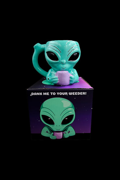 A teal alien figurine and its packaging with the phrase “DANK ME TO YOUR WEEDER!” against a black background.
