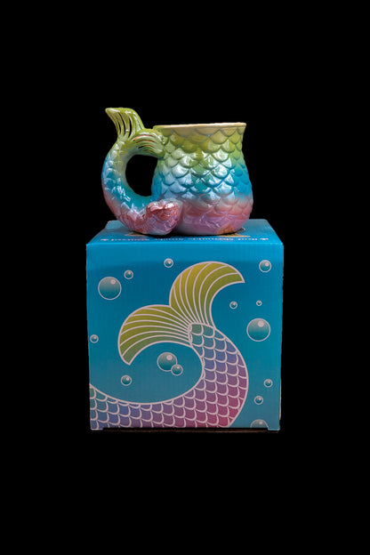 A colorful, iridescent glass water pipe shaped like a mermaid tail rests on top of its matching patterned box.