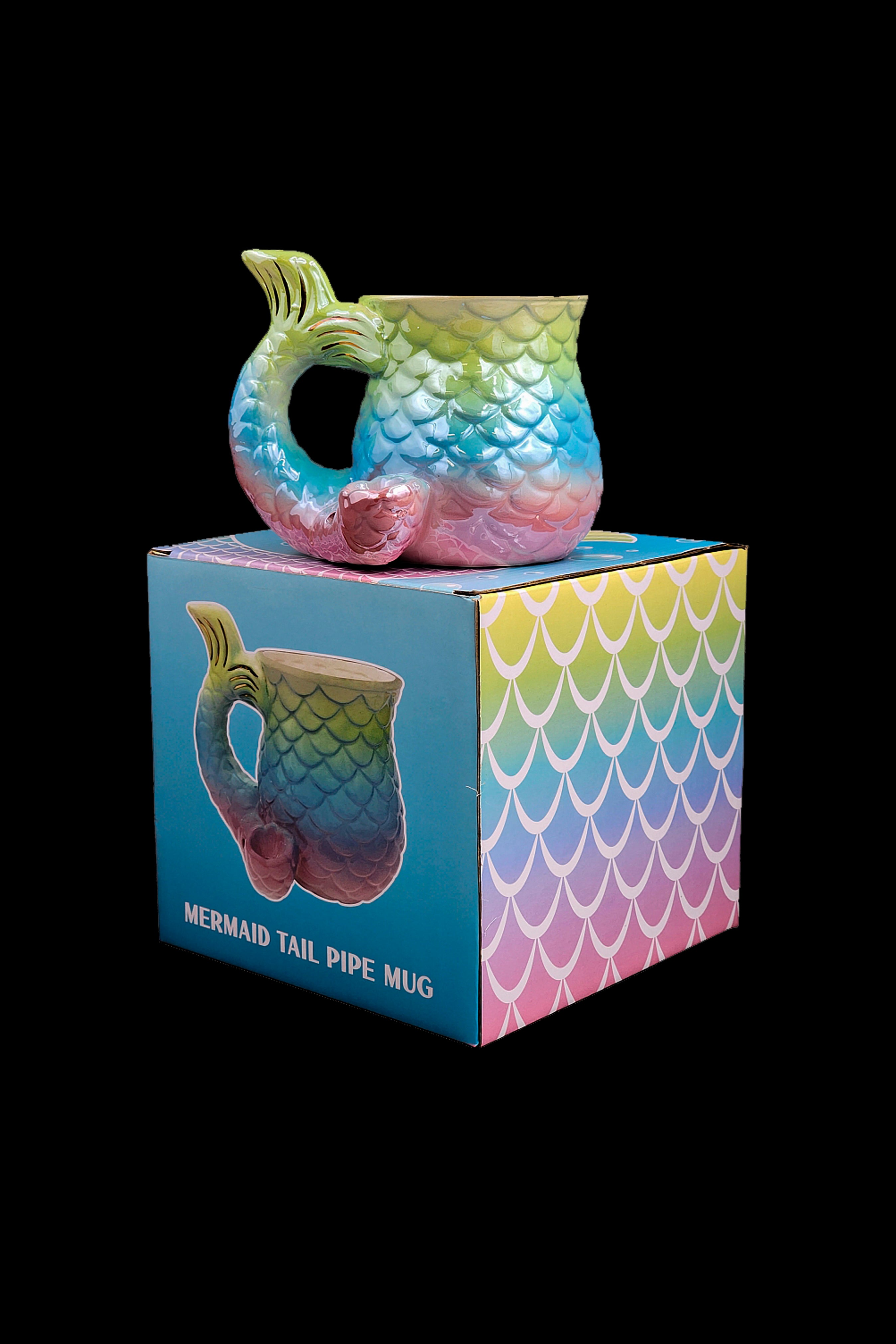 A colorful, mermaid-tail shaped glass pipe rests on its patterned box, labeled “Mermaid Tail Pipe Mug.”