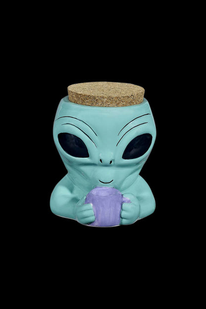 Turquoise alien-shaped ceramic jar with a cork lid, holding a purple crystalline object.