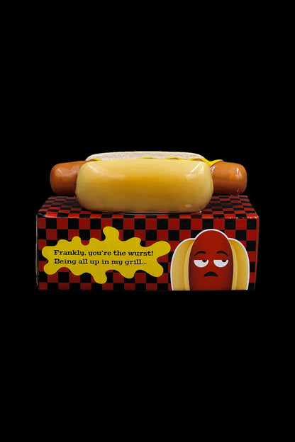 Hot dog-shaped cannabis grinder with text reading "Frankly, you're the wurst! Being all up in my grill..." on a patterned box.