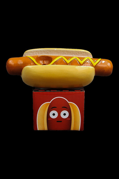 A whimsical, hot dog-shaped silicone container with a smiling face, topped with a realistic-looking hot dog and bun, likely used to conceal cannabis accessories."