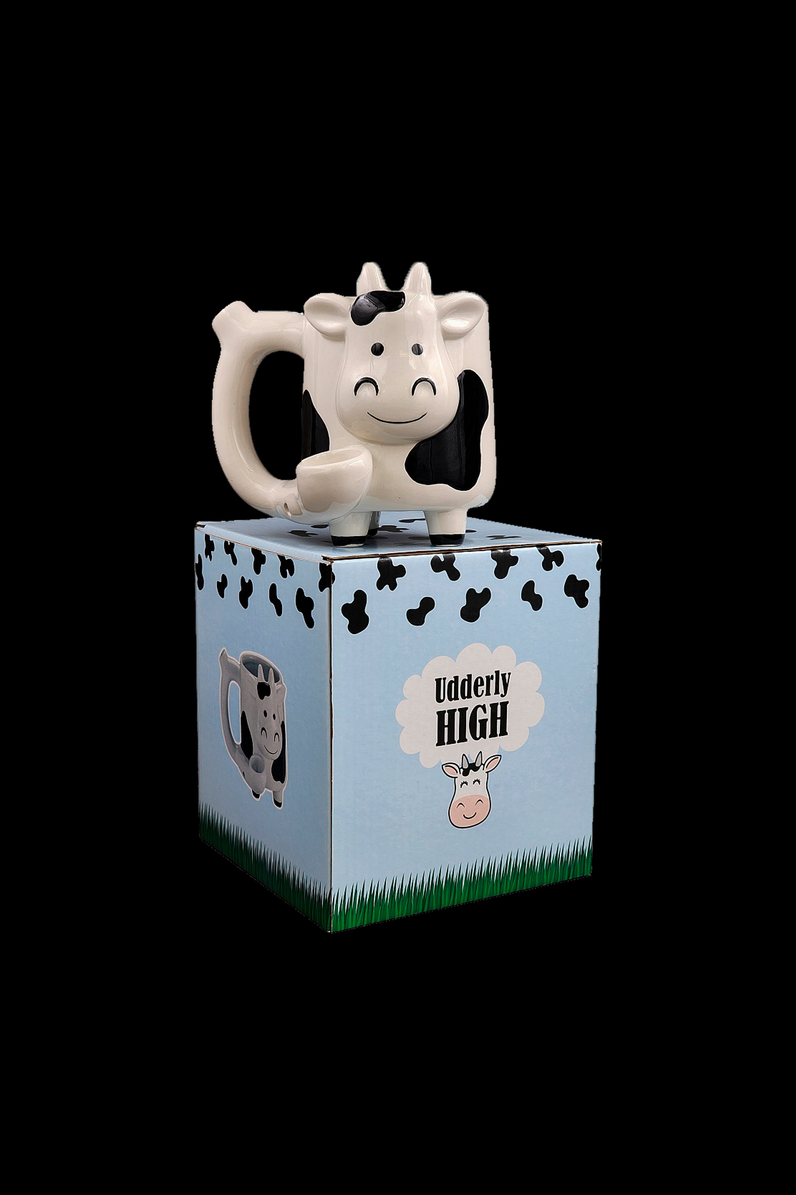 Cow-shaped cannabis accessory atop a blue box with cow print and text reading "Udderly High."