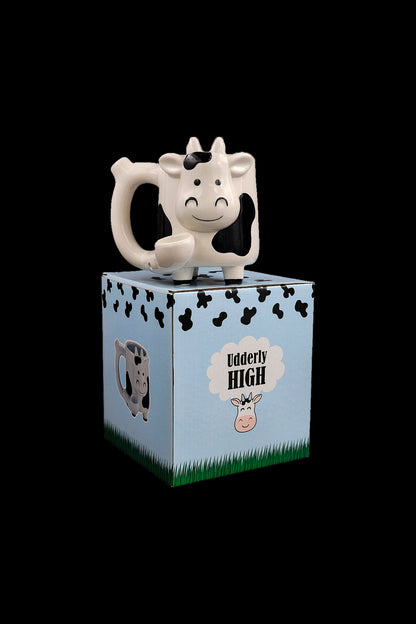 Cow-shaped cannabis accessory atop a blue box with cow print and text reading "Udderly High."