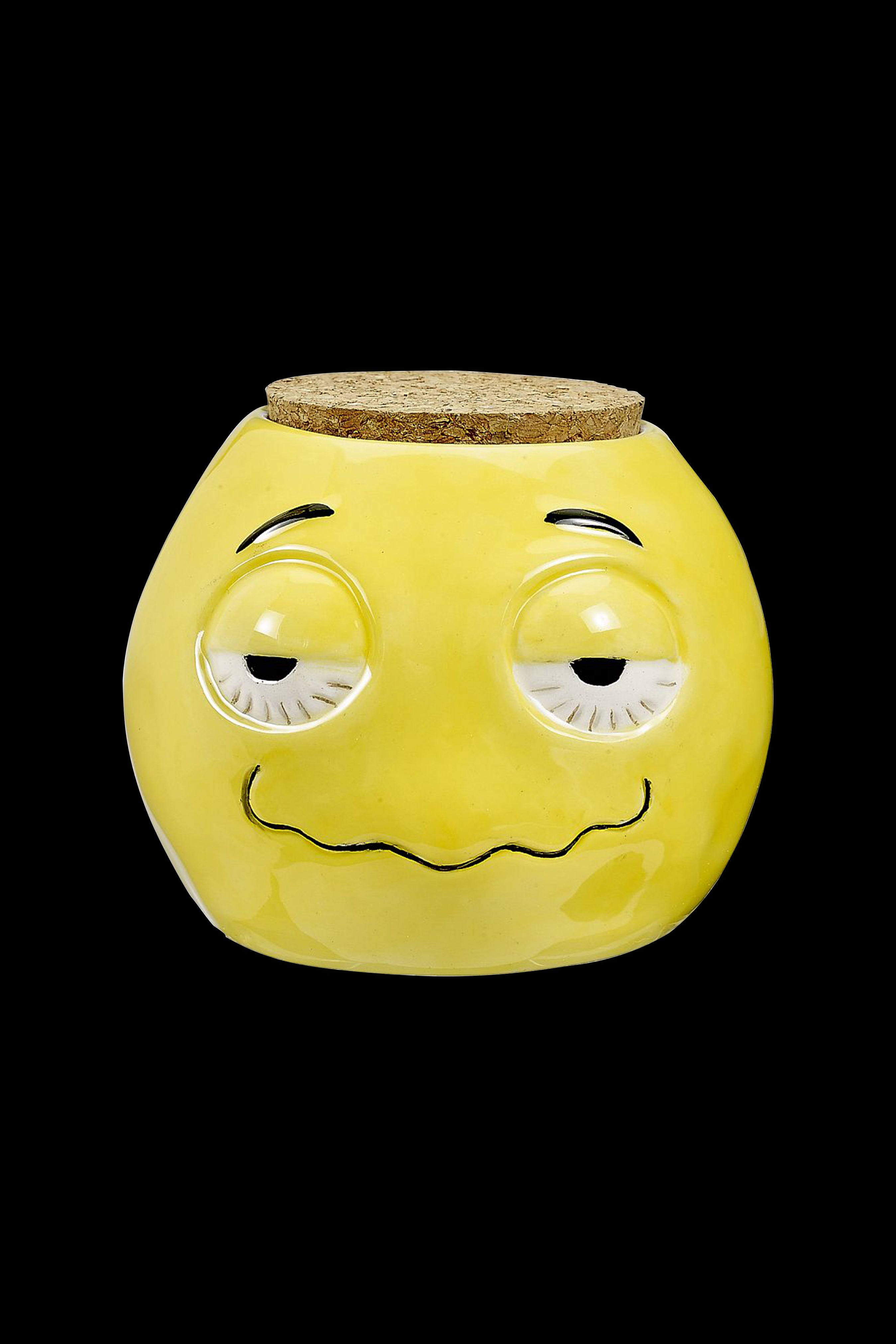 Yellow ceramic jar with a smiling, sleepy face and cork lid, likely for storing cannabis.