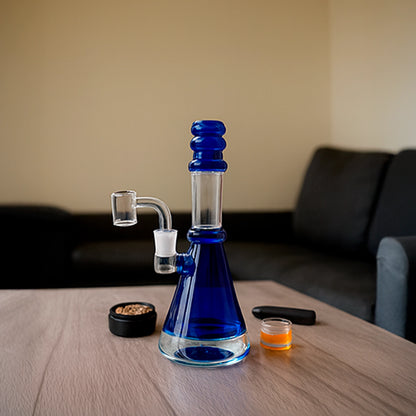 Center-framed shot of a teal Smoke Cartel Transparent Neck Bong w/ Bowl & Banger on a wood table with a couch blurred in the background.